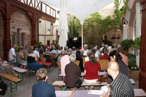 Eine größere Gruppe an Menschen sitzt auf Bänken im Hof des Museum Stadt Miltenberg und lauscht einem Klavierkonzert