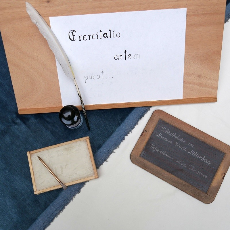 Zu sehen sind ein Schreibpult, Federkiel und Tinte und eine Schiefertafel. Sie sind Bestandteil des Workshops zum Thema mittelalterliche Schreibstube.